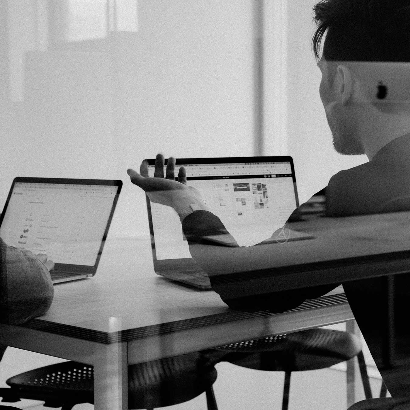two men in a meeting room with laptops in front of them, working on a strategic project.